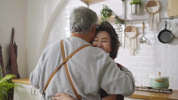 Asian mature senior couple is dancing and smiling in kitchen at home.