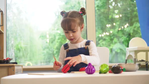 Happy Little girl playing with wooden natural toy food (vegetables) in a children's kitchen. Cute ho