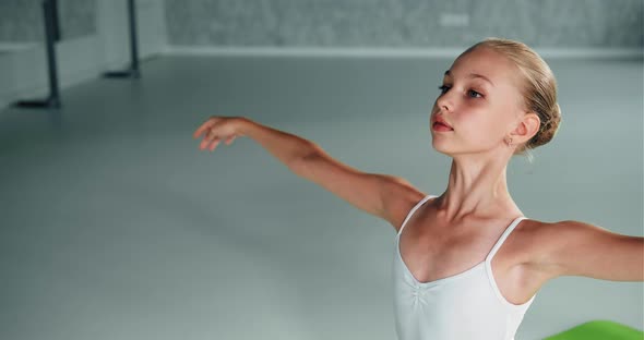 Little Ballerina with Bun on Head Raises Up Hands in Studio