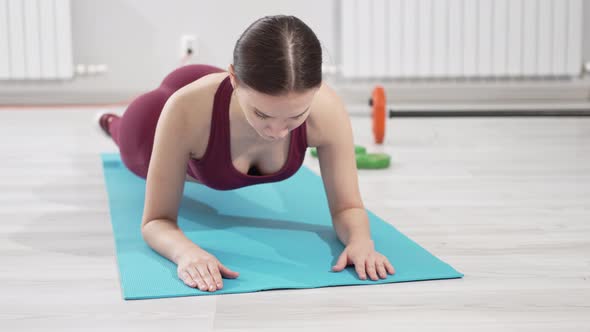 a Beautiful and Slender Woman in a Burgundy Tracksuit Exercises on a Mat