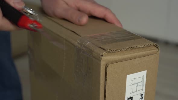 Close Up Mans Hands Open Cardboard Box with Knife at Home Inteerior