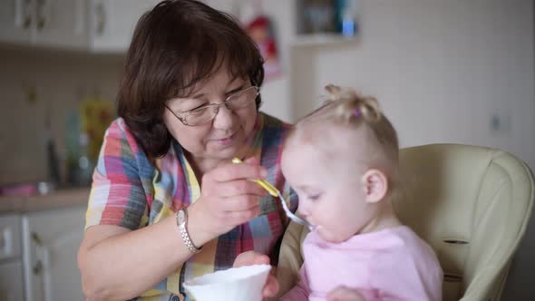 grandmother feeds her granddaughter in the kitchen with a spoon, selective focus