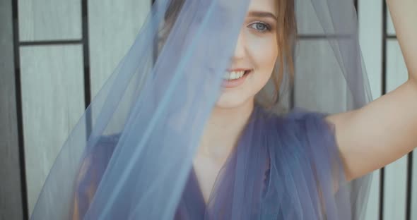 Portrait of  Young lady standing against the wall with a light gray flying dress.