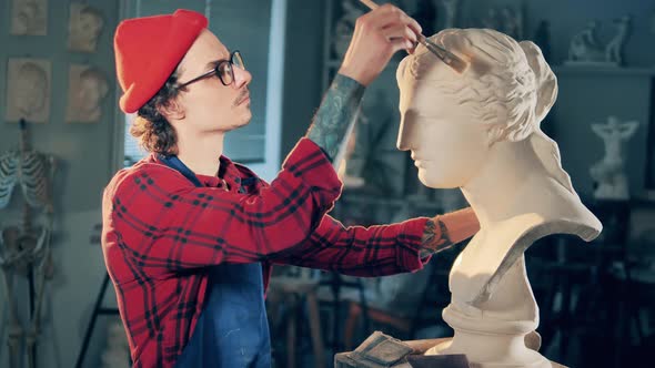 Male Sculptor is Brushing a White Gypsum Bust