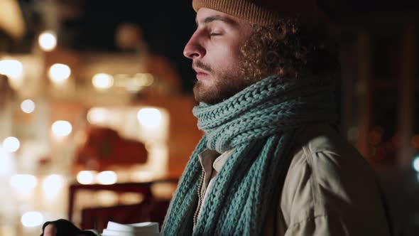 Handsome curly-haired man smoking and drinking coffee outdoors