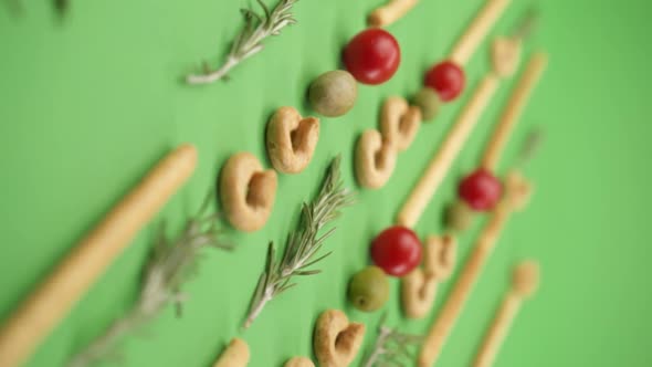 Vertical video: pattern of italian pastries, italian bread sticks, olives, cherry tomatoes, rosemary