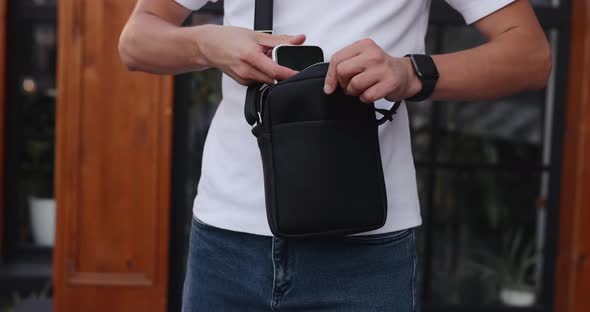 Unrecognizable Man Puts Mobile Phone Into a Messenger Bag