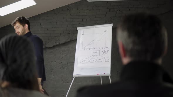 Handsome Young Businessman Pointing at Flipchart During Presentation in Conference Room and Holding