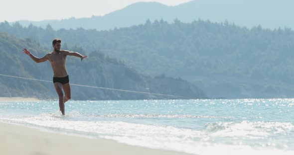 The Handsome Man with a Perfect Athletic Body in Swimming Trunks Having Fun on a Deserted Beach in