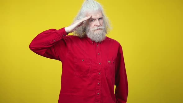 Handsome Confident Senior Man Saluting on Yellow Background Looking at Camera