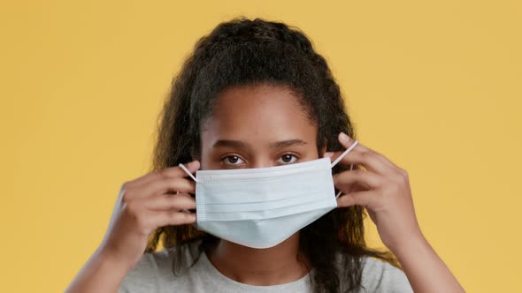 Studio Portrait of Cute African American Girl Teenager Putting on Protective Medical Mask and