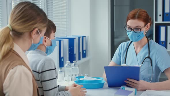 Good Physician Talking to Little Patient Sitting in Mom Arms Family Medical Doctor in Mask and