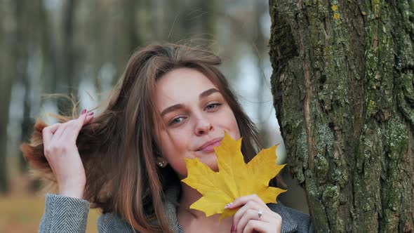 Beautiful Happy Young Girl with a Smile Holds an Autumn Yellow Leaf Near the Face