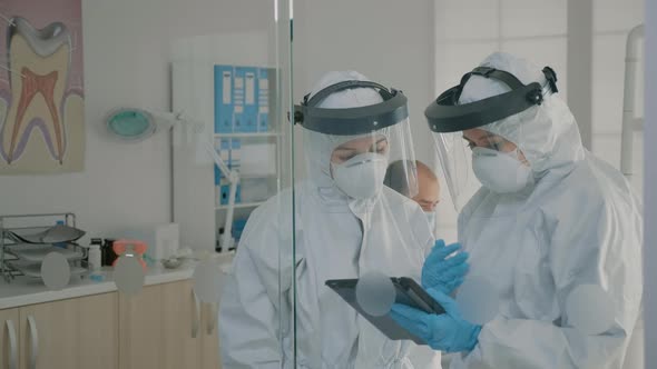 Dentistry Team with Virus Protection Suits Analyzing Digital Tablet