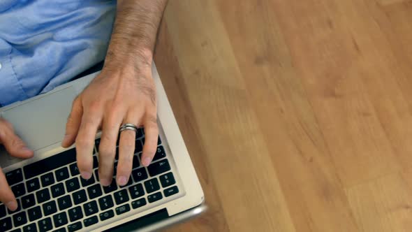 Mid-section of man sitting on floor and using laptop