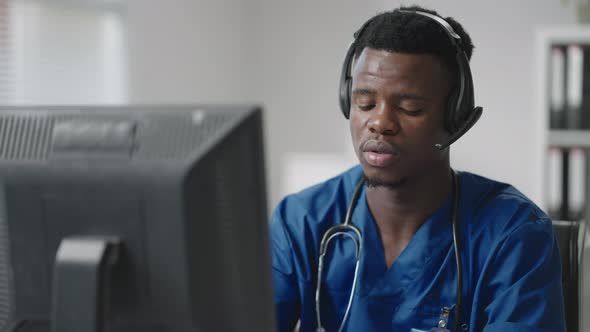 Afroamerican Male Doctor or Nurse with Headset and Computer Working at Hospital 