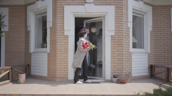 Adult Grandson and His Grandmother Holding Bouquet of Tulips Overlook the Porch of the Big House