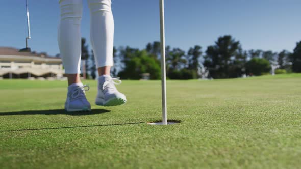 Caucasian female golf player reaching for a ball standing on golf field