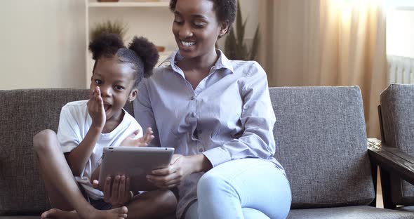 Young Mother with Her Cute Daughter Looking in Digital Tablet Mother Teaches Child African American