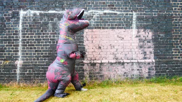 Funny prehistoric dinosaur costume stopping and looking up alongside brick wall