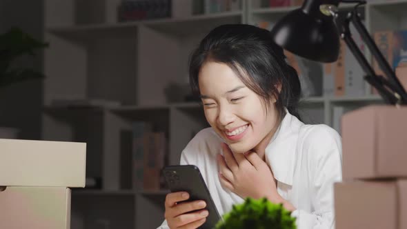 Happy Asian young woman getting messages from customer on smartphone, having new online orders
