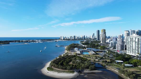 Rising drone view showing an Olympic Aquatic Centre constructed on a coastal strip next to a urban c