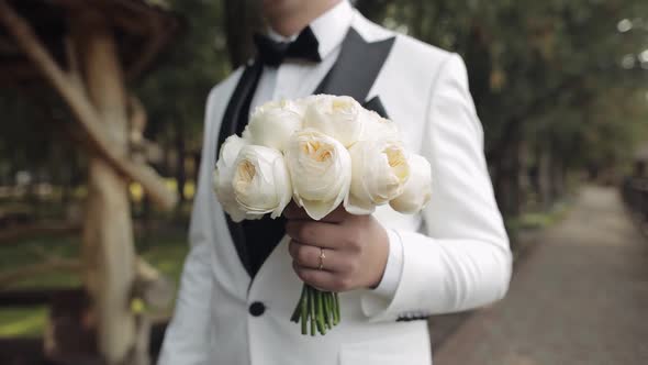 Groom Standing at the Park Alley with a Wedding Bouquet Waiting to His Beloved Bride First Meeting