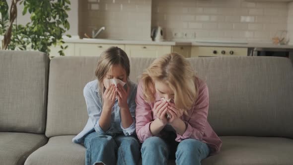 Sad Caucasian Mother and Daughter with a Cold are Sitting at Home on the Sofa with Napkins Sneezing