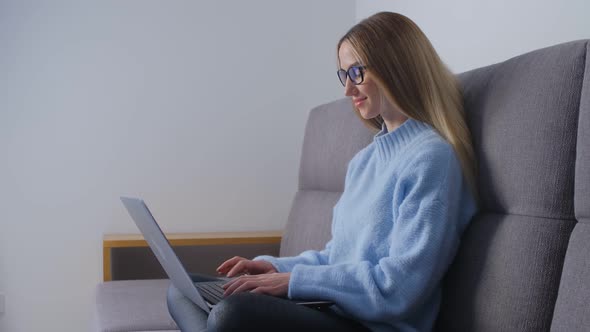 Focused freelancer woman typing text on laptop keyboard while sitting on sofa in apartment in 4k