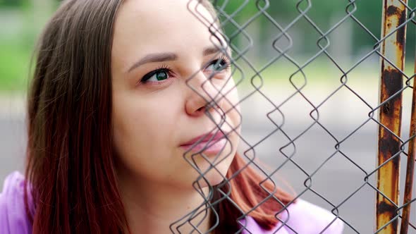 Young Woman with Short Hair in Purple Shirt Looking Away Through Hole of Lattice Fence