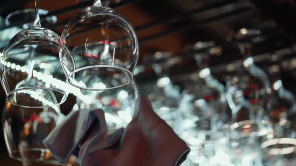 Clean wine glasses hanging upside down above a bar rack in restaurant. Bartender wipes glasses