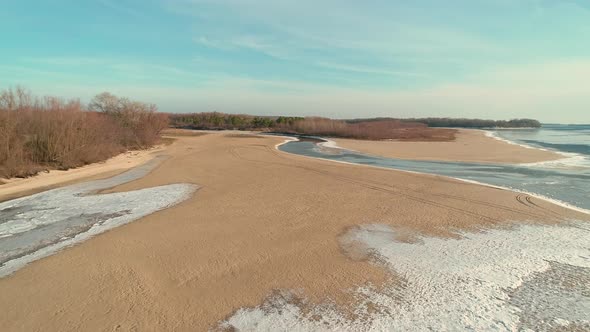 Aerial Drone Footage of Flight Over a Sandy Shore with a Small River in Winter