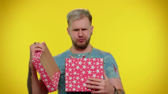 Young Man Unwrapping Birthday Gift and Expressing Disappointment Dislike Bad Present Dissatisfied