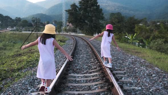 Two cute Asian girls balancing on the railroad tracks with their arms outstretched.