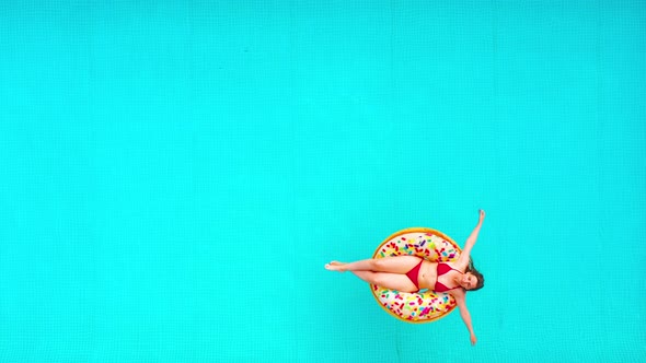 Aerial View of a Woman in Red Bikini Swimming on a Donut in the Pool