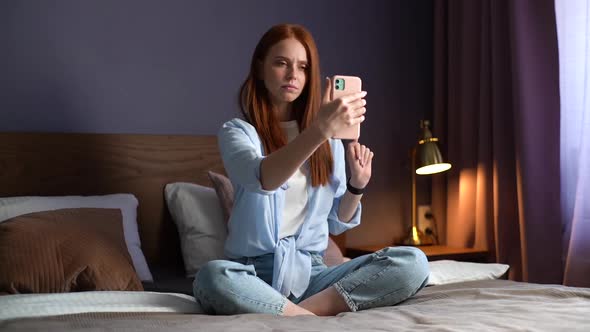 Pretty Redhead Young Woman Listens Carefully To Partner During Online Video Chat Sitting on Bed.