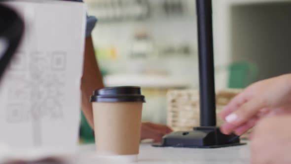 Video of hands of biracial waitress serving coffee and holding payment terminal