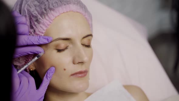 A cosmetologist injects Botox shots into the wrinkle area of a beauty woman.