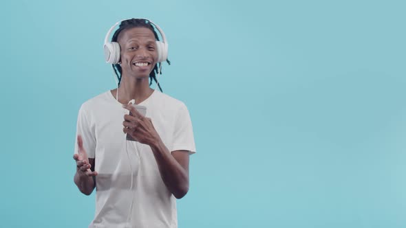 Black positive man with headphones emotionally sings holding phone in hand and smiling