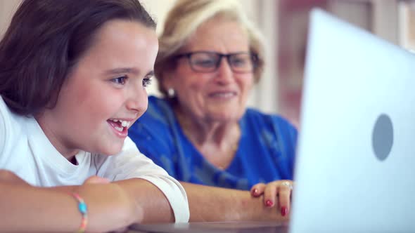 Positive girl teaching grandmother watching videos on laptop at home