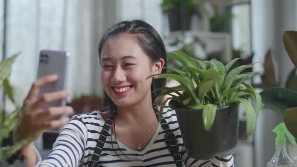 Close Up Of Smiling Asian Woman Holding The Plant And Taking Photo By Smartphone At Home