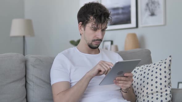 Casual Young Man Relaxing on Couch and Browsing Internet on Tablet