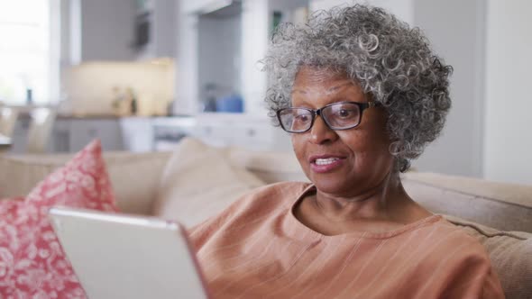 Senior african american woman having a video chat on digital tablet while sitting on the couch at ho