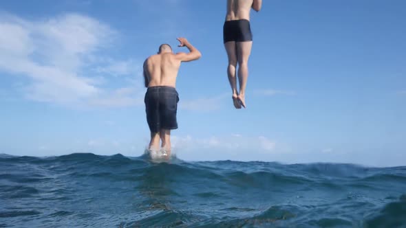 Rear View of Two Young Men Falls Into the Blue Ocean on Summer with Sky View.