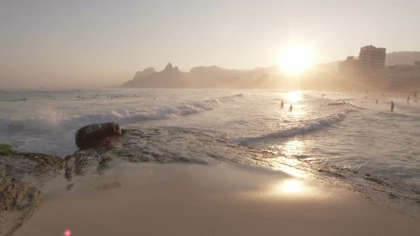 Slow motion, sunset shot of white waves rolling onto beach as people swim