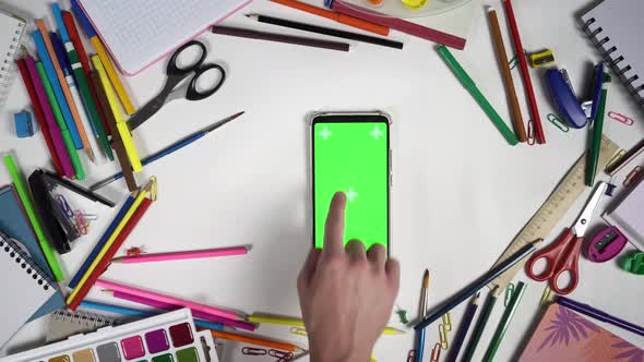 Composition of School Accessories Surrounding Smartphone with Greenscreen and Man Tapping on Display