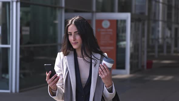 Happy businesswoman with travel mug using smartphone in the street