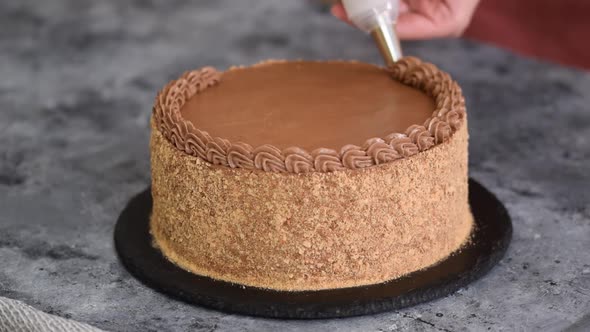 Woman Decorating Cake with Chocolate Cream Holding Pastry Bag in Kitchen