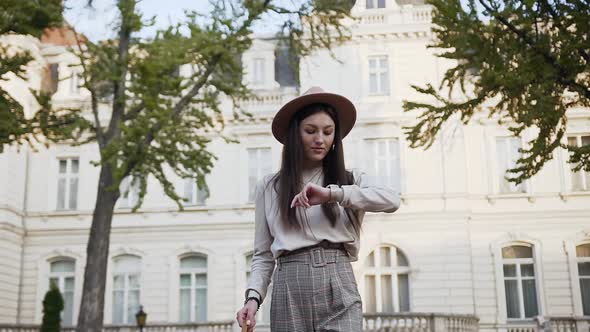 Beautiful Young Woman in Stylish Hat Walking Near the Luxurious Mansion on Sunny Day