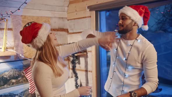 Happy Young Couple Dancing with Christmas Lights and Santa Hats